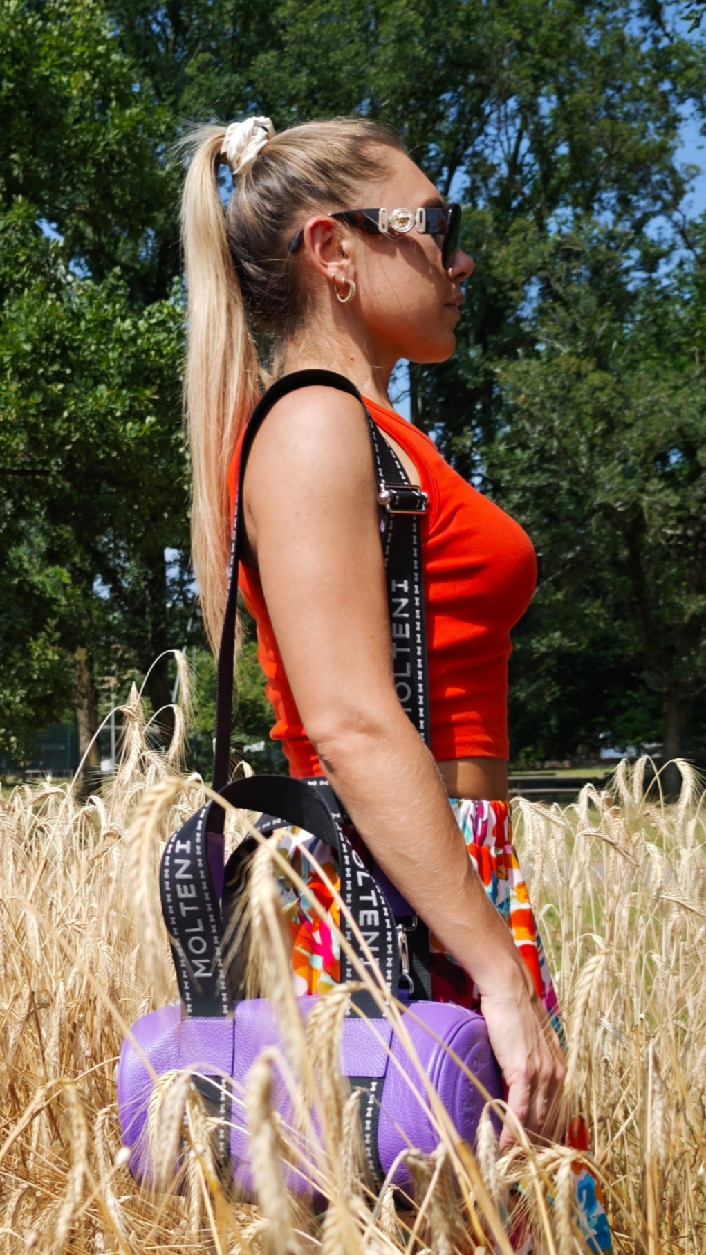 Modella che indossa NORA small viola a tracolla nel campo di grano