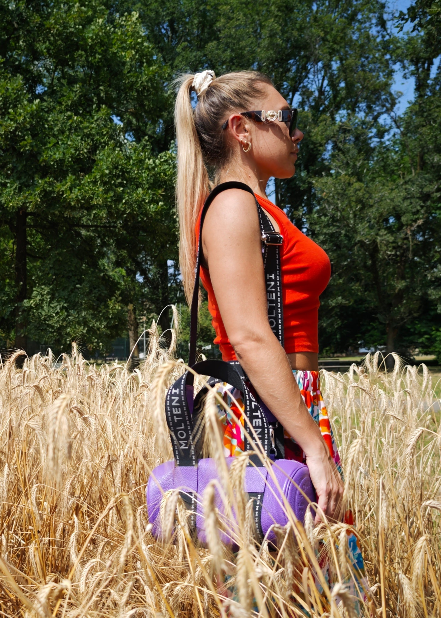 Modella che indossa NORA small viola a tracolla nel campo di grano